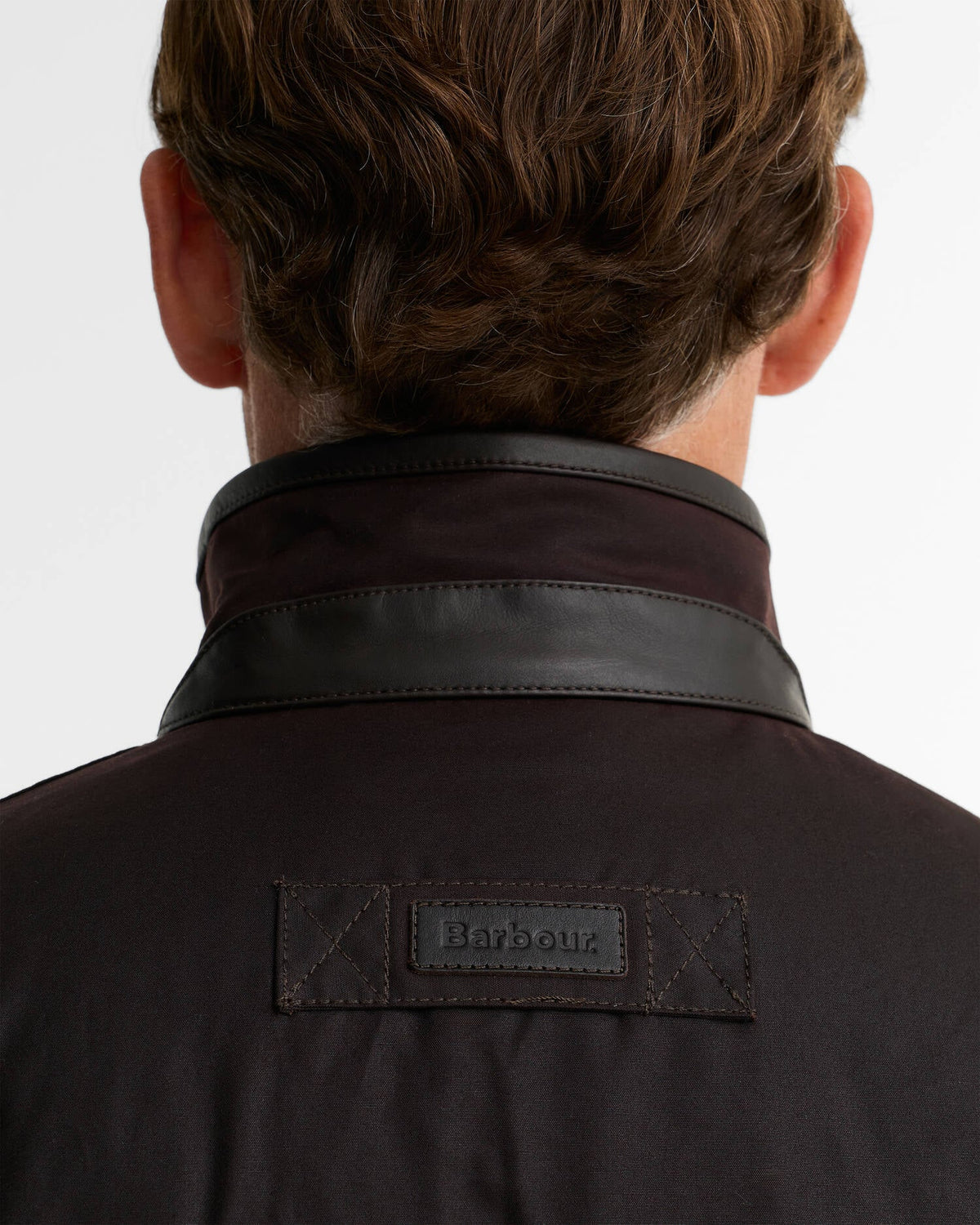 Back view of a person wearing a dark brown Barbour jacket with a contrasting black leather collar and a Barbour brand patch on the back.