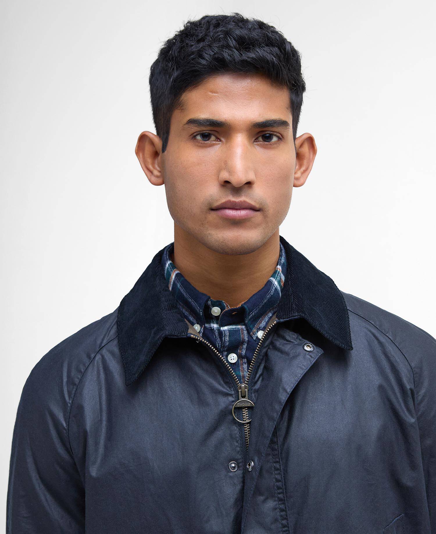 Man wearing a dark blue jacket over a plaid shirt on a white background