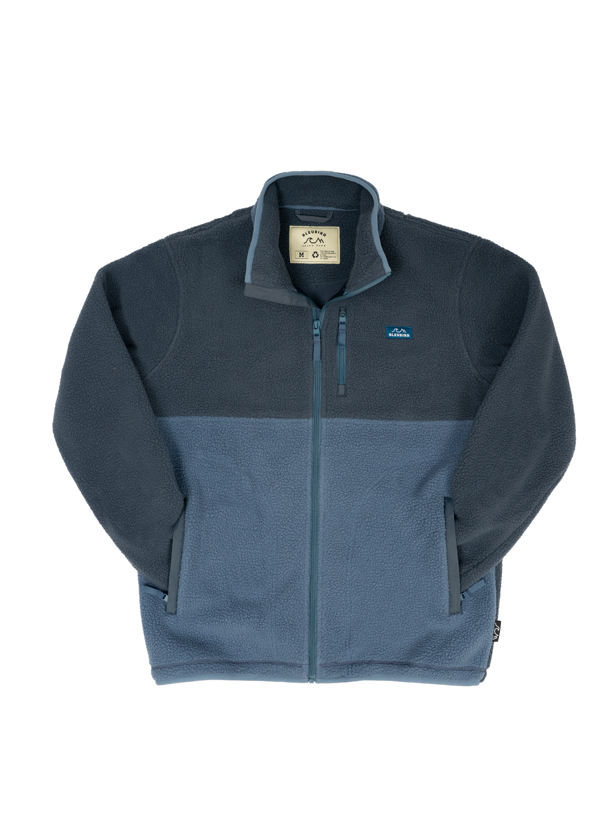 A colorblock fleece jacket from Bleubird, featuring a dark slate blue upper section and a muted blue lower section, with a full-zip front and a small logo on the left chest.