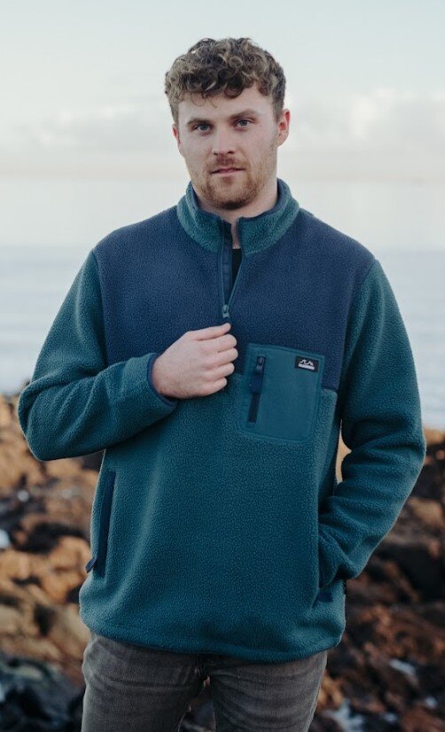 Man wearing a teal fleece pullover standing outdoors with a scenic background