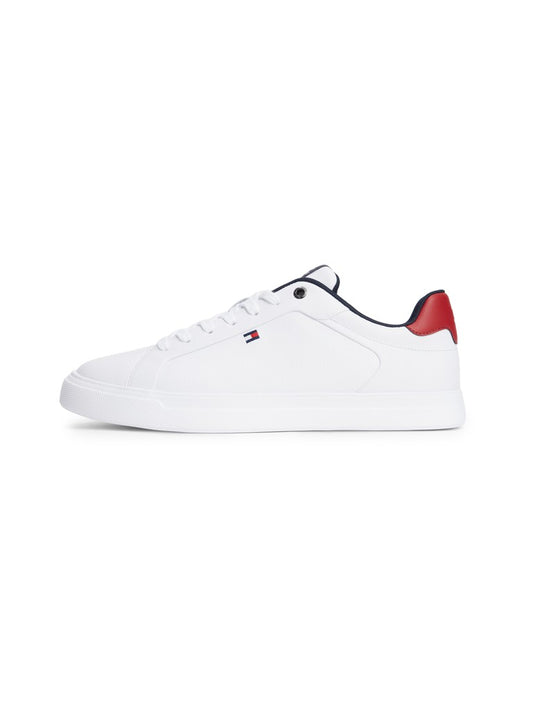 A white low-top sneaker by Tommy Hilfiger, featuring a small red and navy flag logo on the side, a red heel tab, and navy lining, shown against a plain white background.