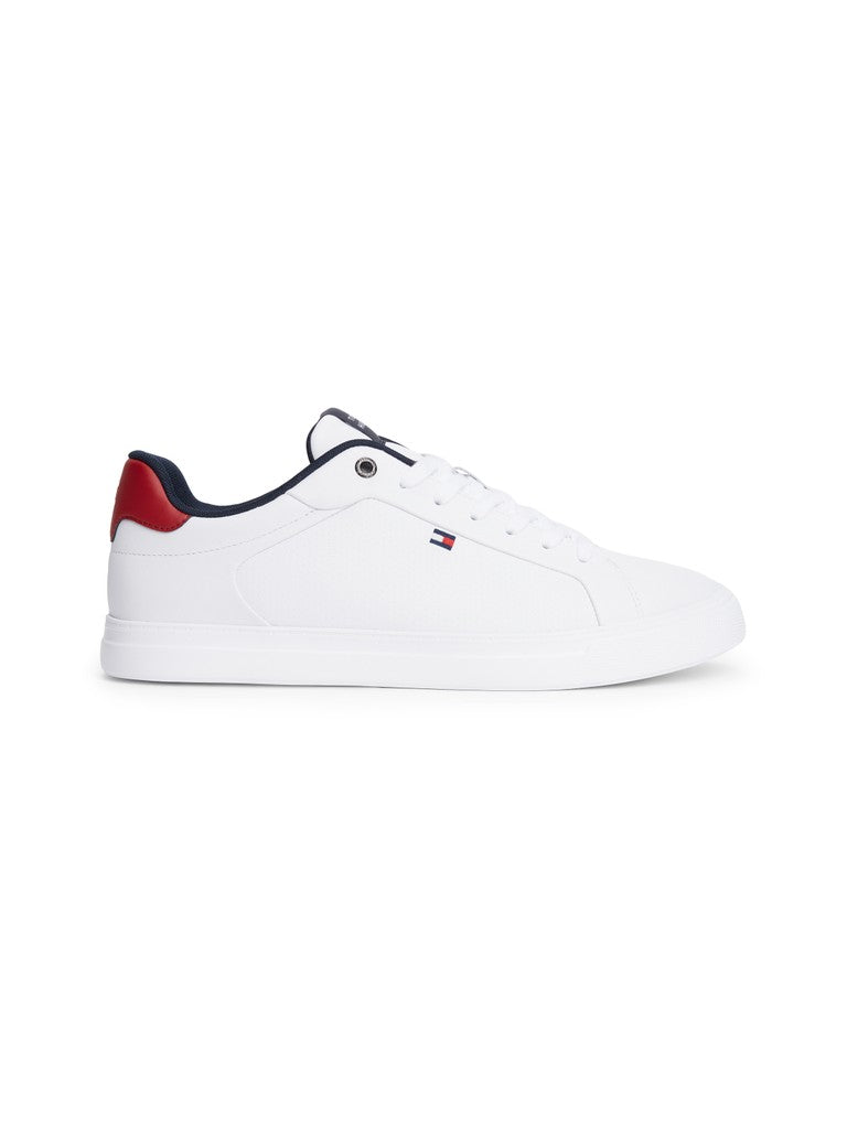 A white low-top sneaker by Tommy Hilfiger, featuring a red heel tab, navy blue lining, and the signature Tommy Hilfiger flag logo on the side, set against a plain white background.