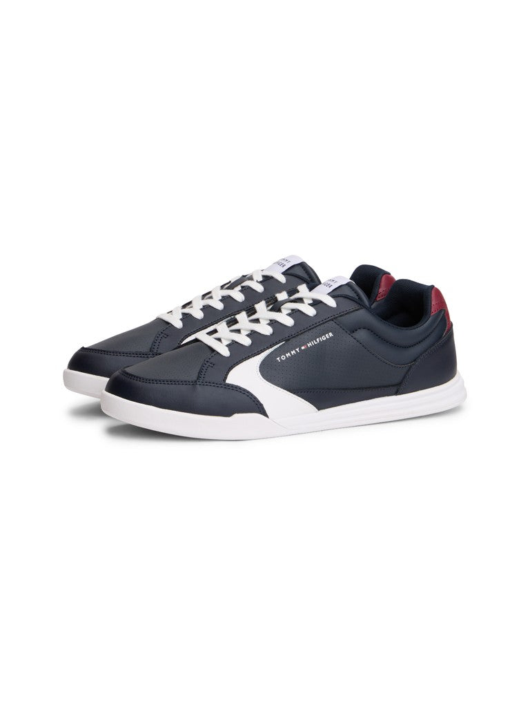 A pair of low-top Tommy Hilfiger athletic sneakers in navy blue and white, featuring white laces, a white side stripe, and a small red accent on the heel tab, shown against a plain white background.