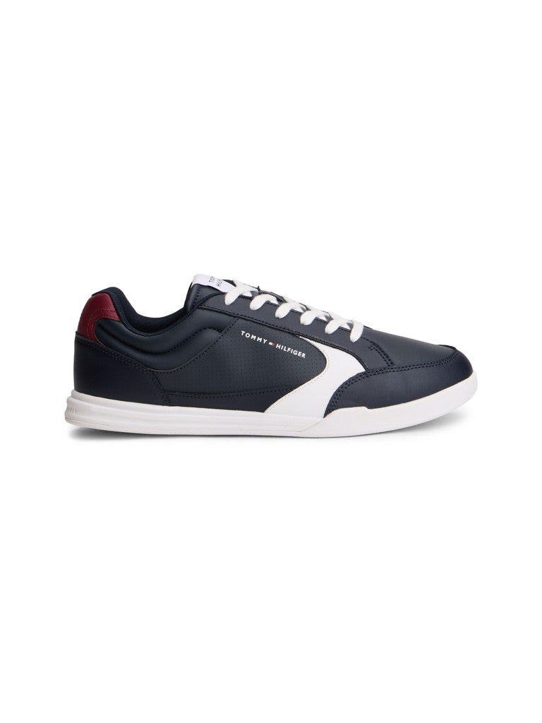 A low-top sneaker by Tommy Hilfiger in navy blue and white, featuring a white side stripe, white laces, and a small red accent on the heel tab, shown against a plain white background.