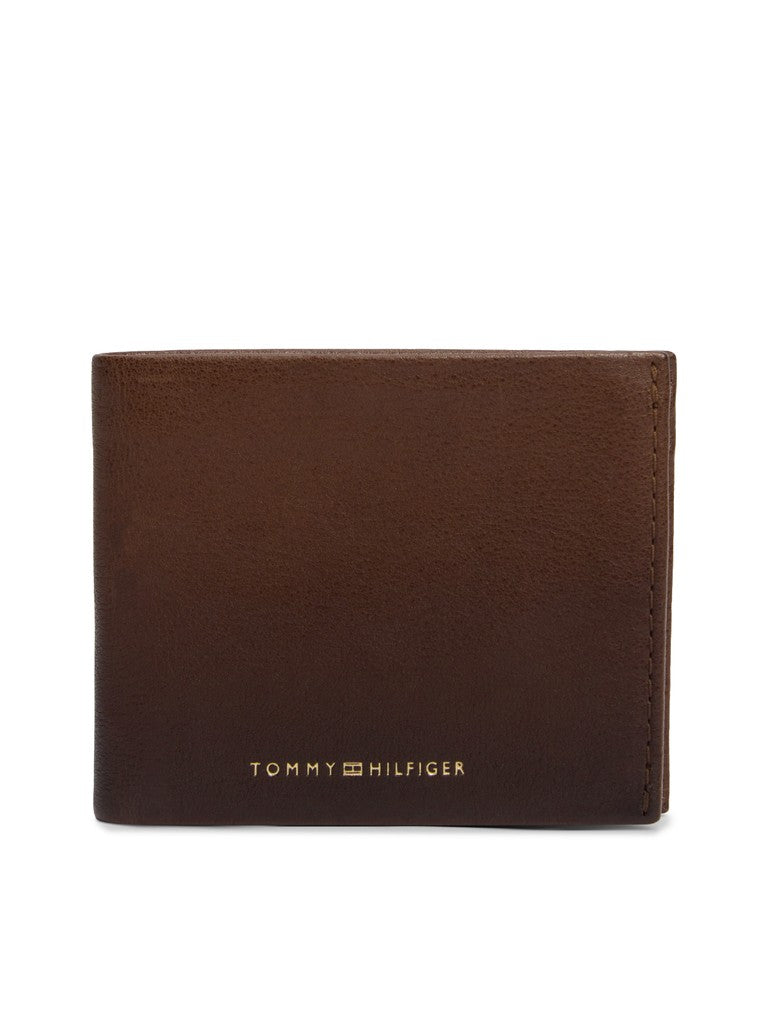 A brown leather bifold wallet with gold-toned 'TOMMY HILFIGER' branding on the front, shown against a plain white background.