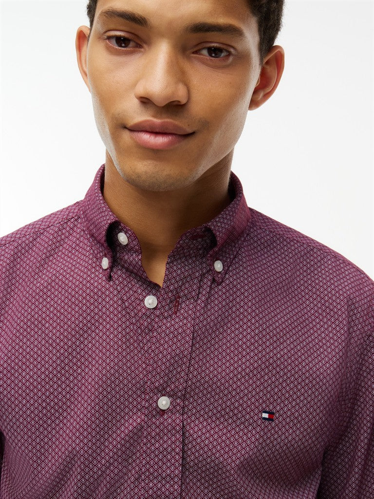 A close-up of a man wearing a Tommy Hilfiger button-down shirt in a textured purple and white micro-pattern. The Tommy Hilfiger flag logo is visible on the left chest.