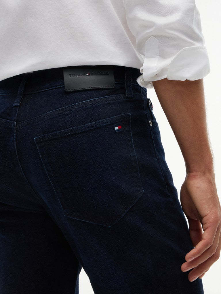 Close-up of a person wearing dark navy blue Tommy Hilfiger jeans with a white shirt tucked in, showing the back pocket and brand tab.