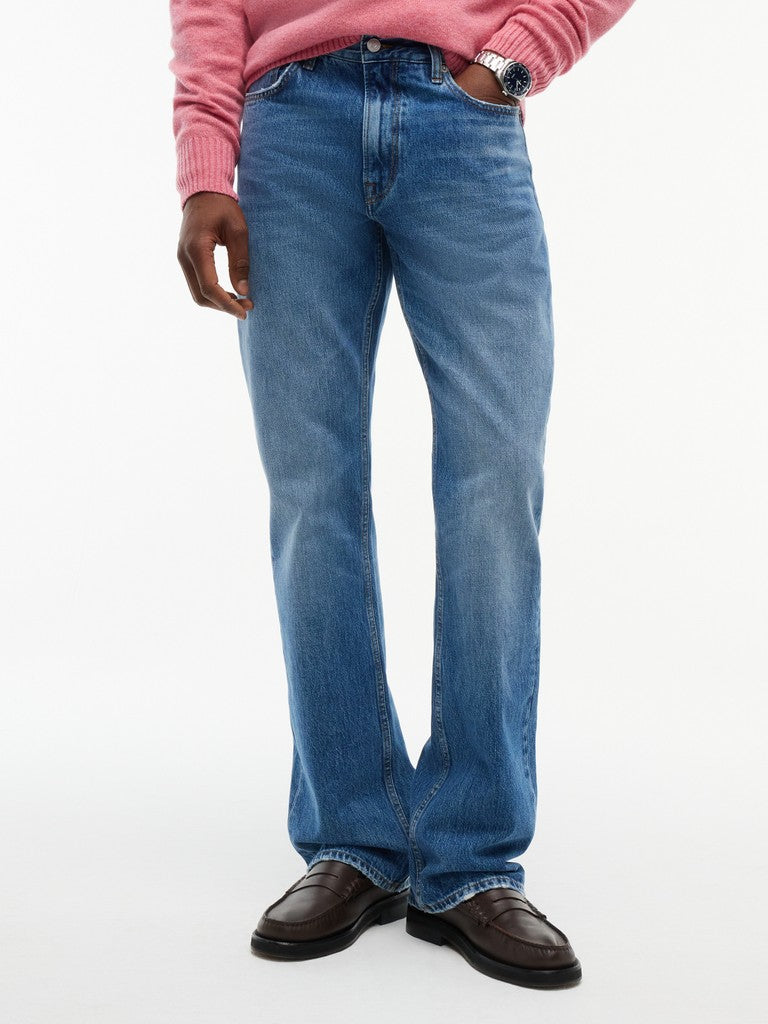 A person wearing medium-wash blue jeans with a pink ribbed sweater and dark brown leather loafers, shown from the waist down against a plain white studio background.