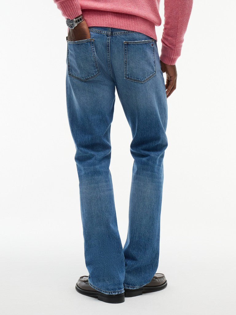 Rear view of a person wearing medium-wash blue jeans, a pink ribbed sweater, and black shoes against a plain white studio background.