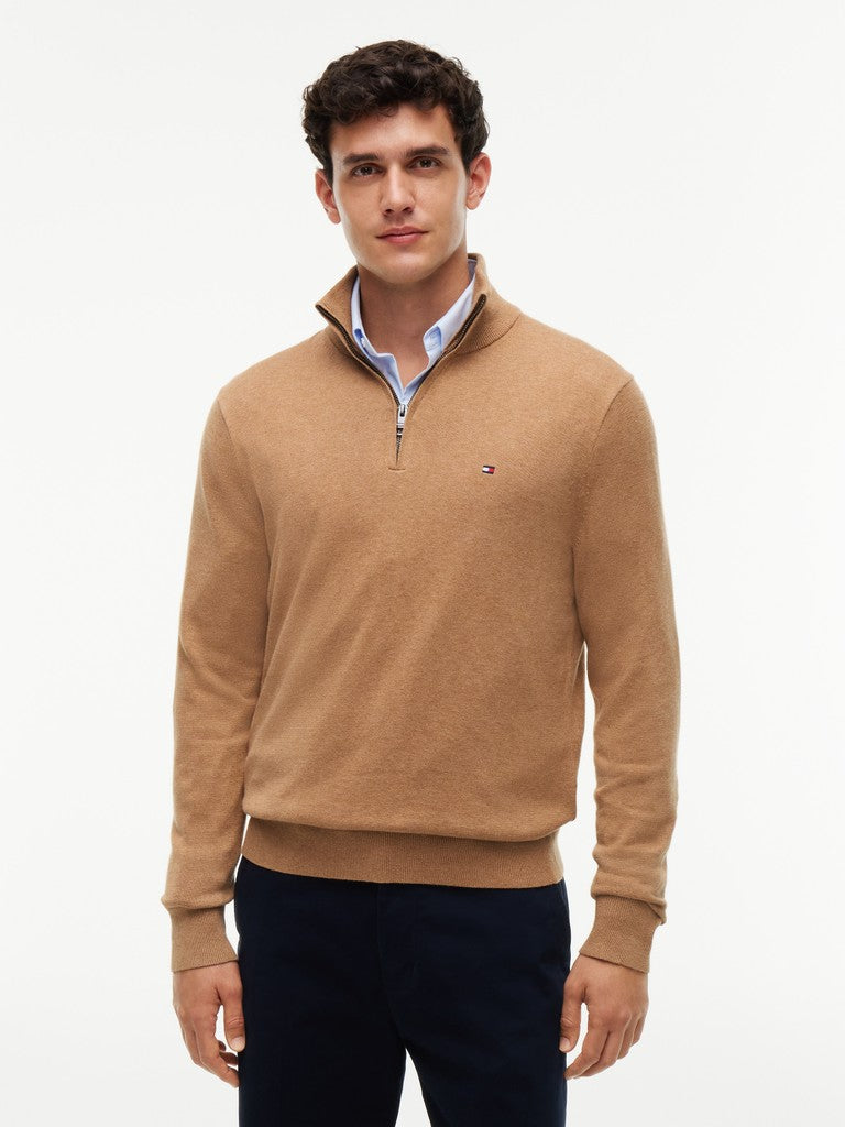 A close-up of a man wearing a tan quarter-zip sweater by Tommy Hilfiger over a white collared shirt, against a clean white background.