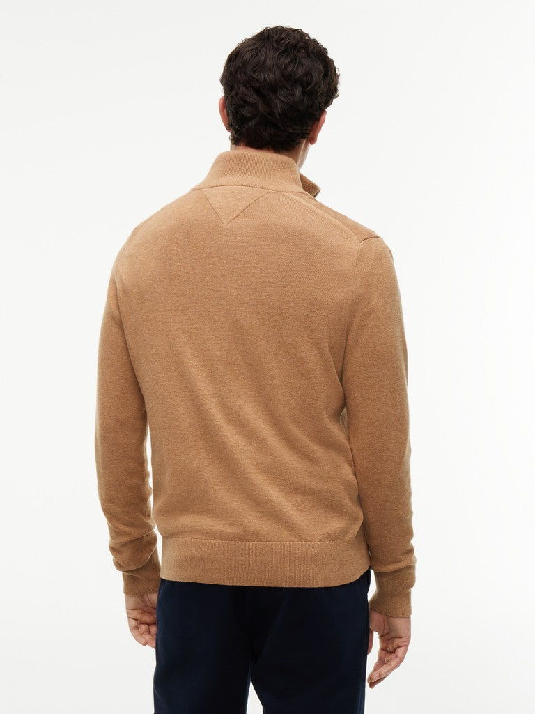 Back view of a man wearing a tan quarter-zip sweater by Tommy Hilfiger and navy trousers, against a clean white background.