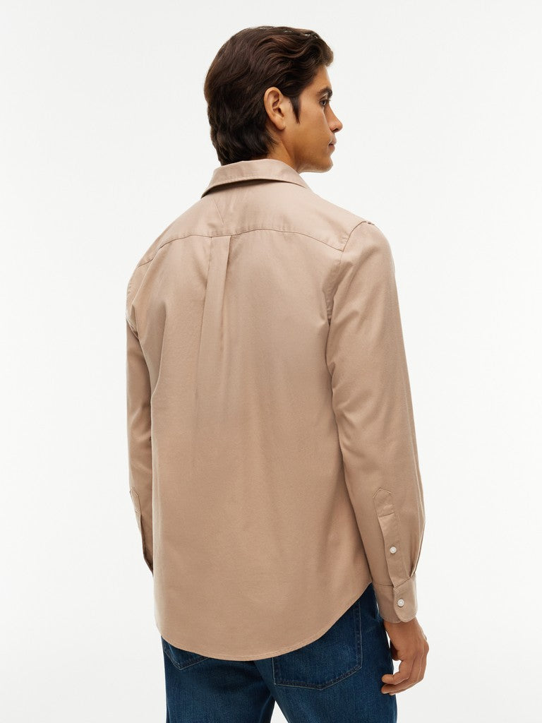 A man wearing a beige long-sleeve button-down shirt, shown from a rear three-quarter view against a plain white studio background.