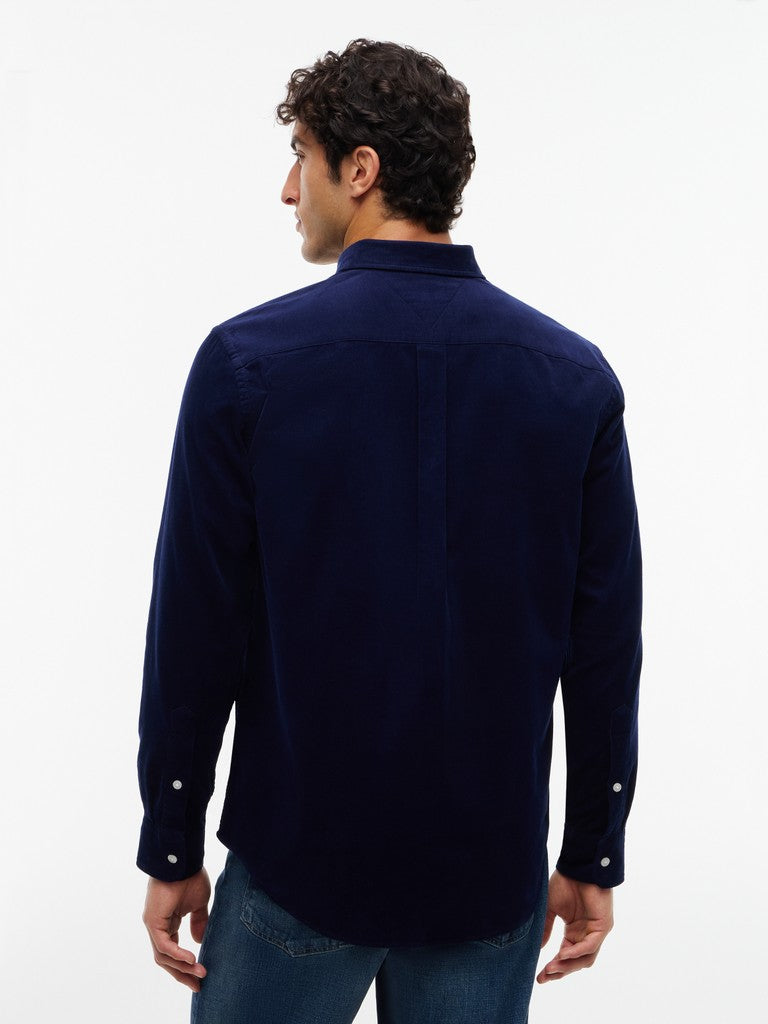 A man viewed from the back wearing a dark navy blue long-sleeve button-up shirt and blue jeans against a plain white studio background.