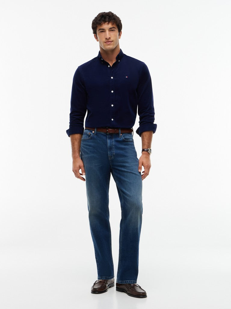 A man modeling a navy blue long-sleeve button-down shirt and blue jeans against a plain white studio background.