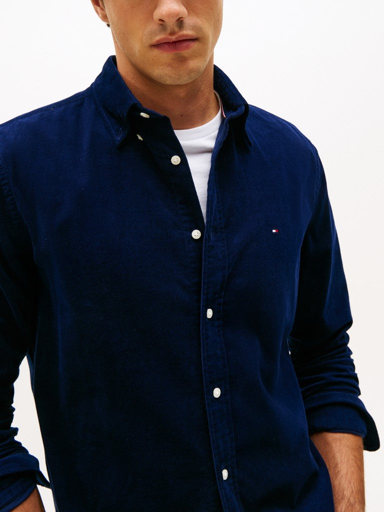 Man wearing a navy blue button-up corduroy shirt over a white T-shirt on a light gray background