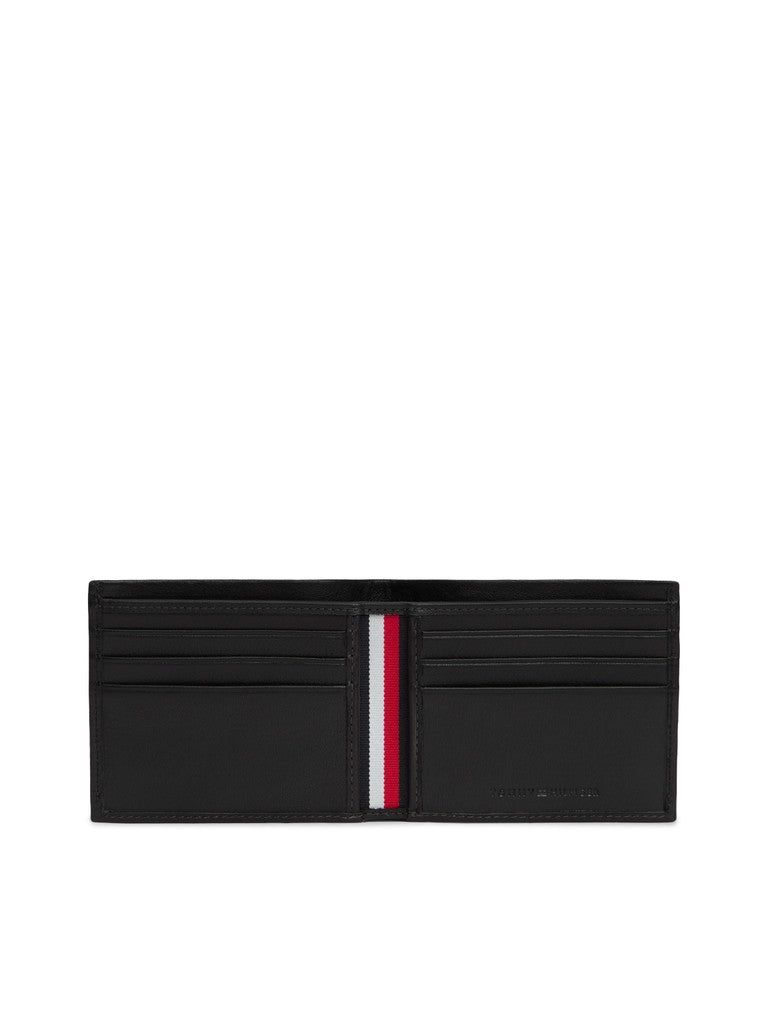 A black leather bi-fold wallet shown open, featuring multiple card slots and a signature vertical tricolor stripe in red, white, and blue down the center. The brand name 'Tommy Hilfiger' is subtly debossed on the lower right corner of the right pocket.