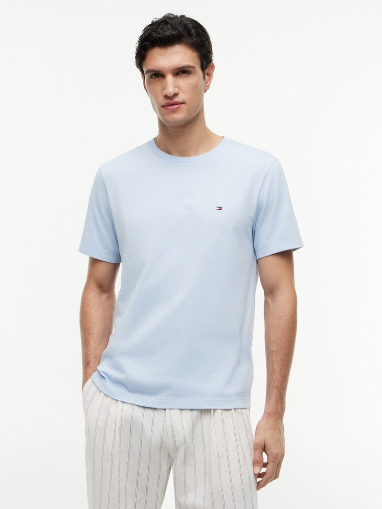 Man wearing a light blue t-shirt with a small Tommy Hilfiger logo on a white background