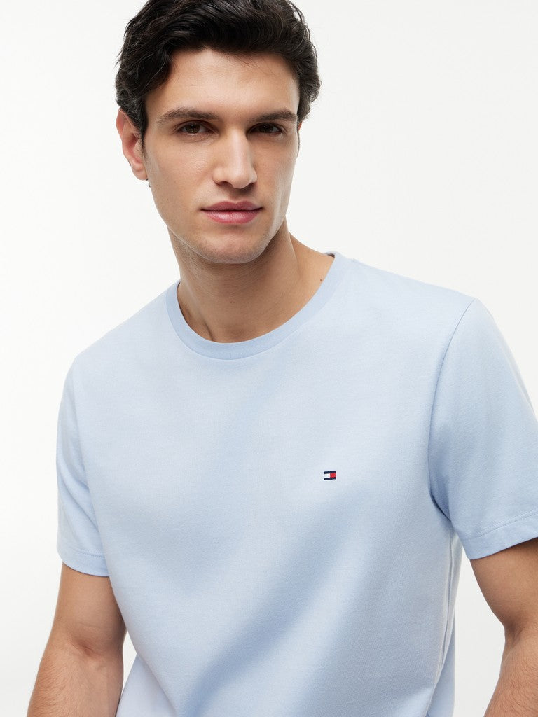 Man wearing a light blue t-shirt with a small logo on a white background