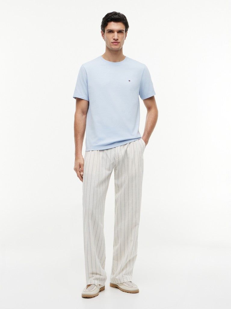 A man modeling a light blue crew-neck t-shirt and off-white pinstriped trousers against a plain white studio background.