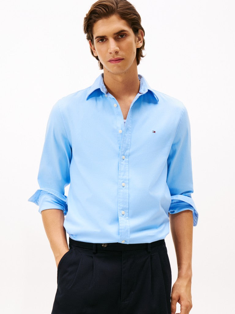 Man wearing a light blue shirt with Tommy Hilfiger Flag logo with rolled-up sleeves on a white background