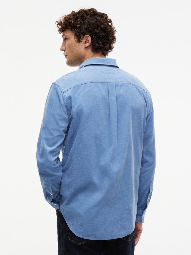 A man wearing a light blue long-sleeve button-down shirt, shown from the back against a plain white background.
