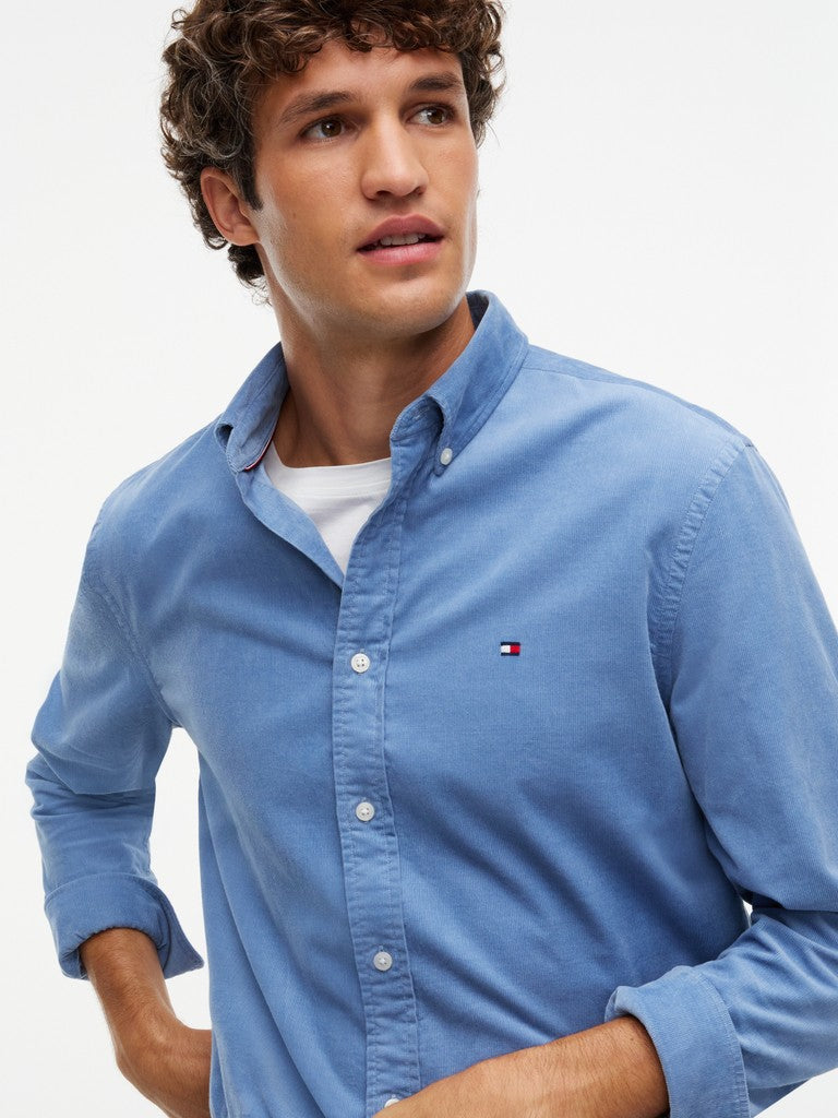 A man wearing a light blue Tommy Hilfiger corduroy button-down shirt over a white undershirt, photographed against a clean white background.