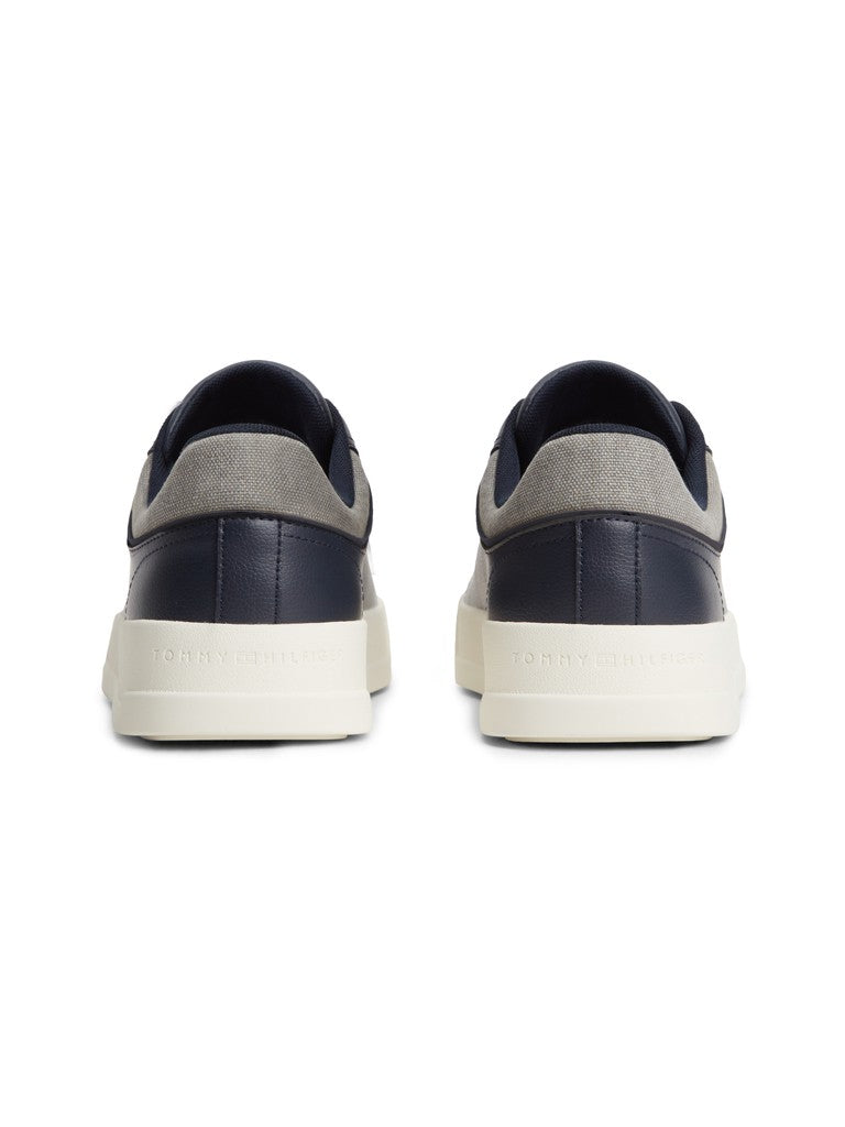 A pair of low-top sneakers shown from the back, featuring navy blue leather and textile panels, a light gray textile side panel, and thick off-white rubber soles with embossed branding.