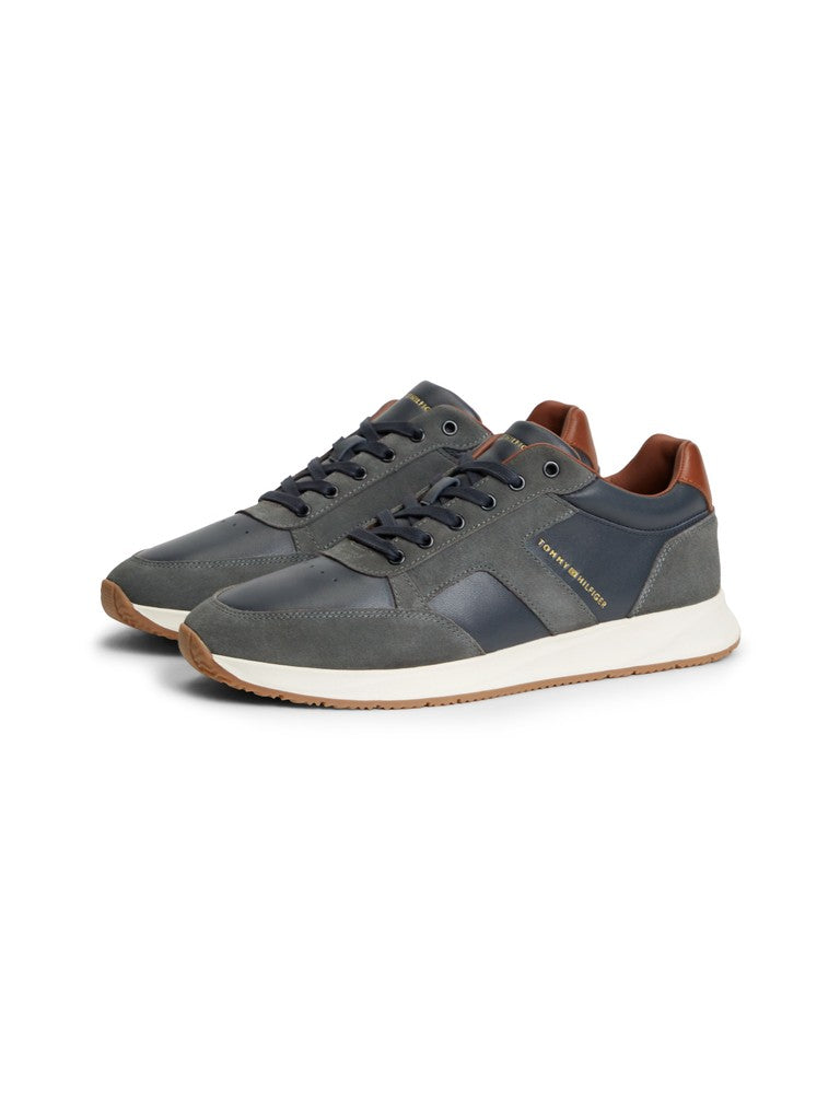 Pair of Tommy Hilfiger leather suede lace up sneakers angled from the side with Tommy Hilfiger logo in gold lettering. Navy and grey panels with brown details