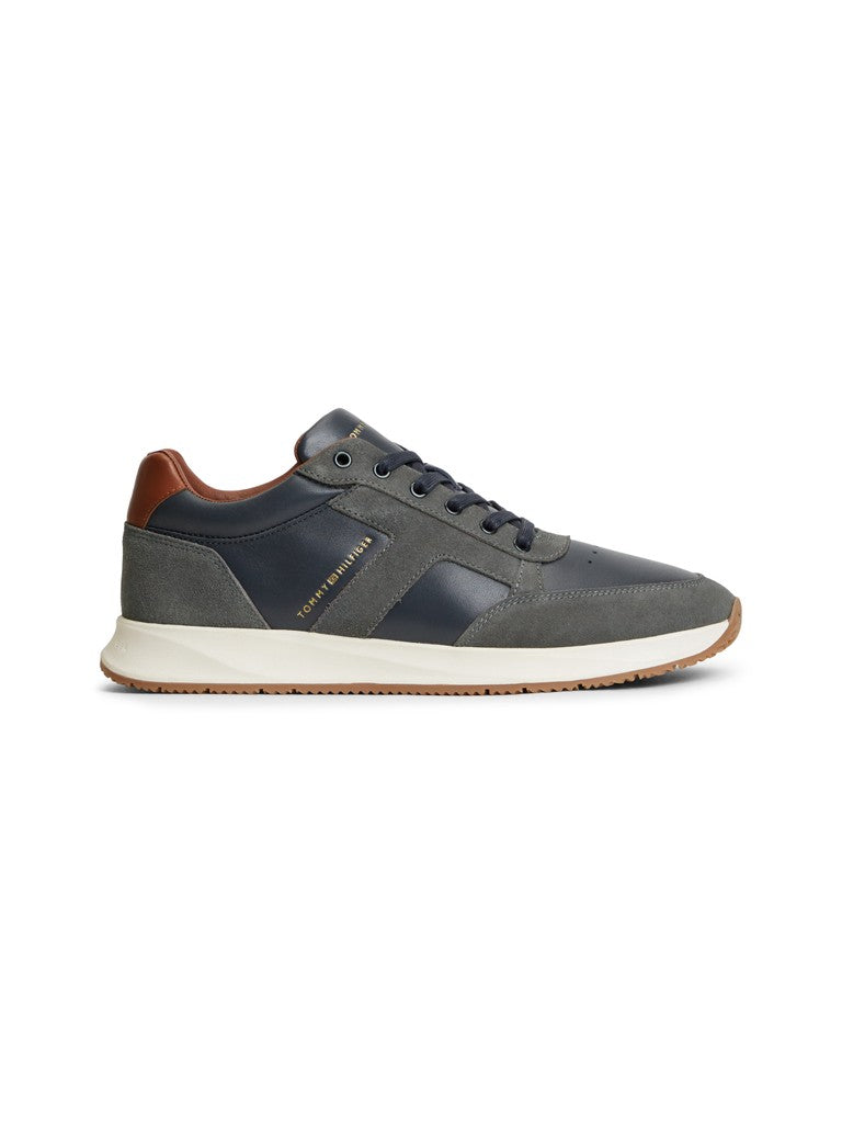 Tommy Hilfiger leather suede lace up sneaker from the side with Tommy Hilfiger logo in gold lettering. Navy and grey panels with white sole and brown details