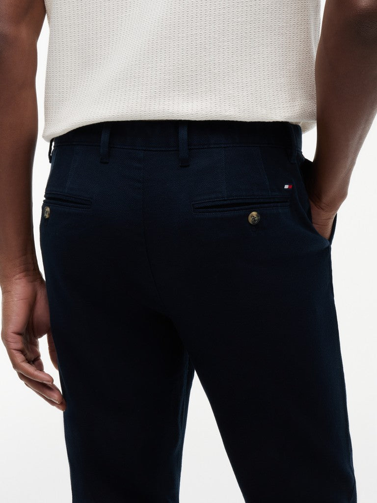 Close-up back view of a person wearing dark navy trousers with a white textured knit top, showing the back pockets and a small Tommy Hilfiger flag logo on the pocket.