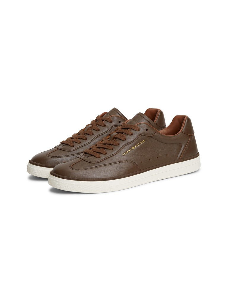 Brown low-top sneakers with Tommy Hilfiger logo on the side and white soles on a light gray background