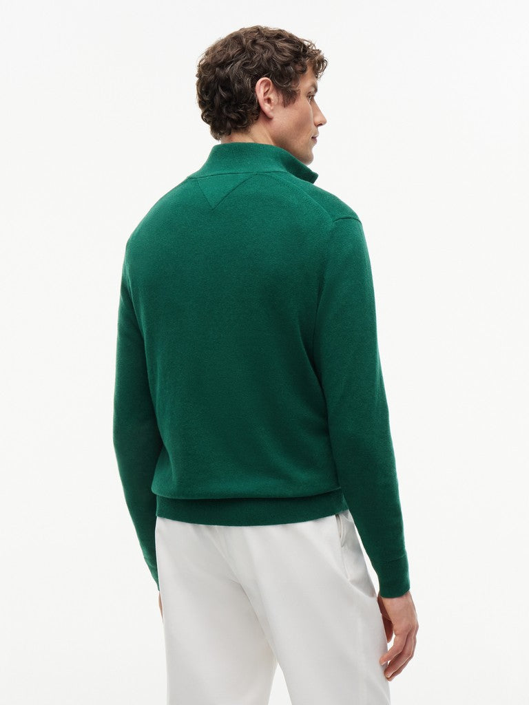 Back view of a man wearing a green quarter-zip sweater by Tommy Hilfiger over a white trousers, against a clean white background.
