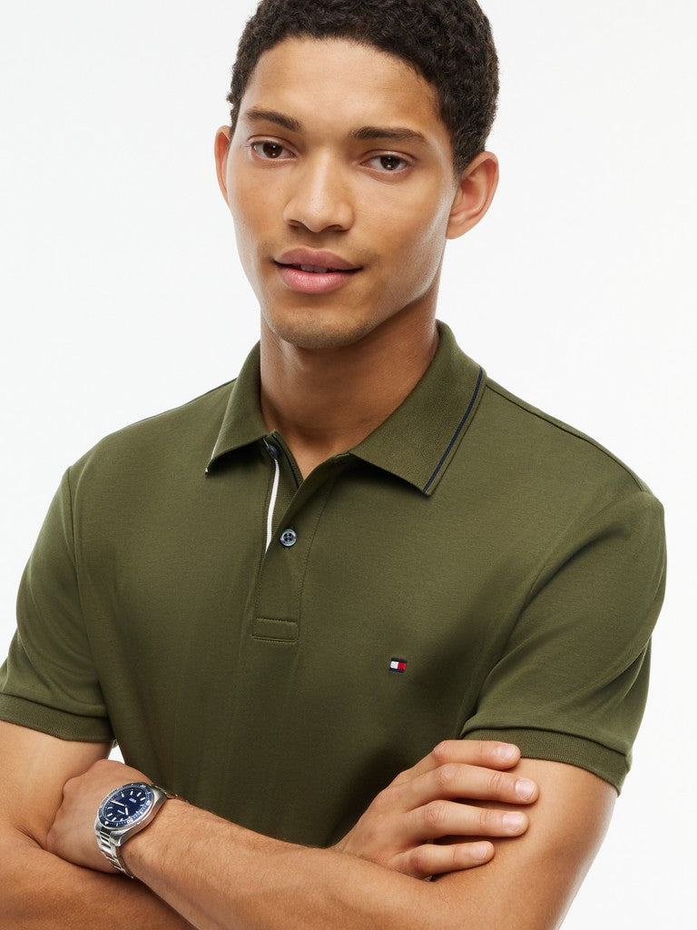 A man wearing an olive green short-sleeve polo shirt with a small embroidered Tommy Hilfiger flag logo on the chest, posed against a clean white background.