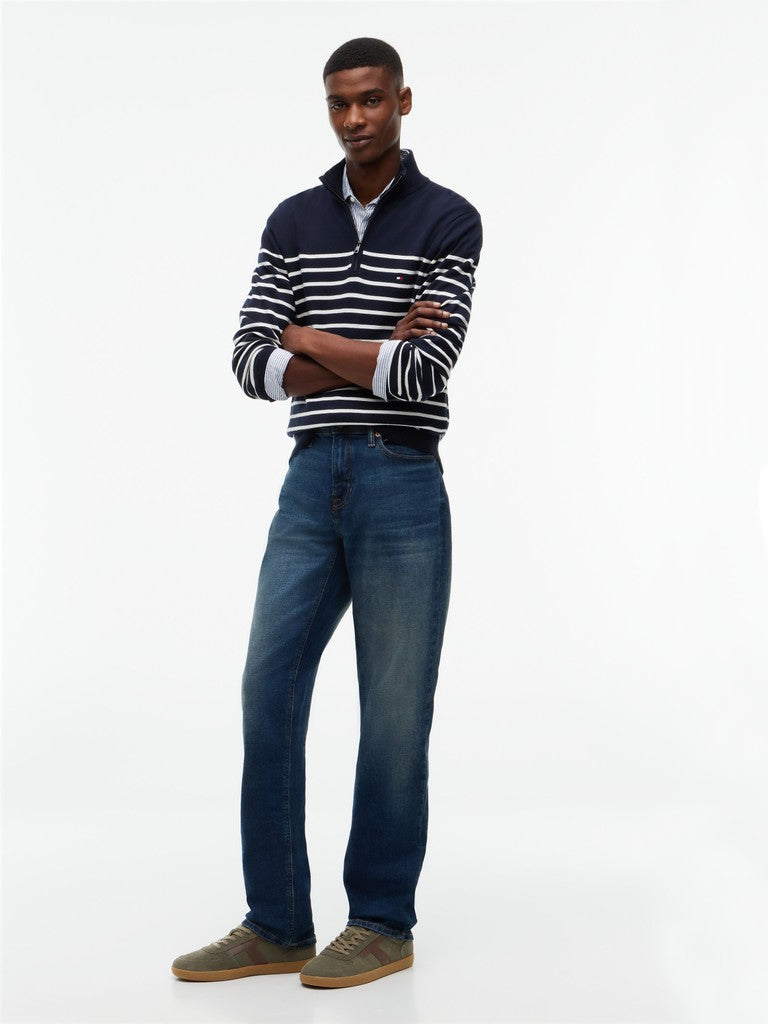 A man modeling a navy blue and white horizontally striped quarter-zip knit sweater, paired with dark blue jeans and green suede shoes, against a plain white studio background.