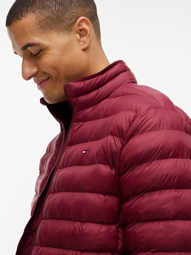 A close-up side profile of a man wearing a maroon quilted puffer jacket against a plain white background.