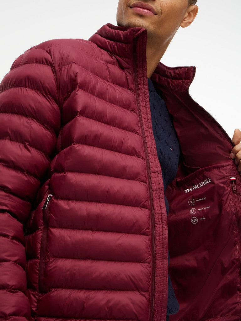 A close-up of a man wearing a maroon quilted puffer jacket, showing the high collar, front zipper, and zippered pockets. 