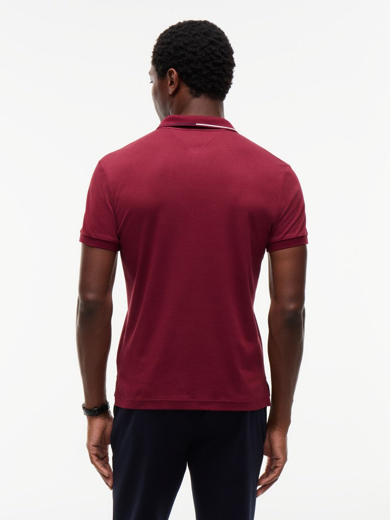 A man viewed from the back wearing a short-sleeve polo shirt in deep burgundy with a thin white stripe detail on the collar, paired with dark navy pants, against a plain white background.