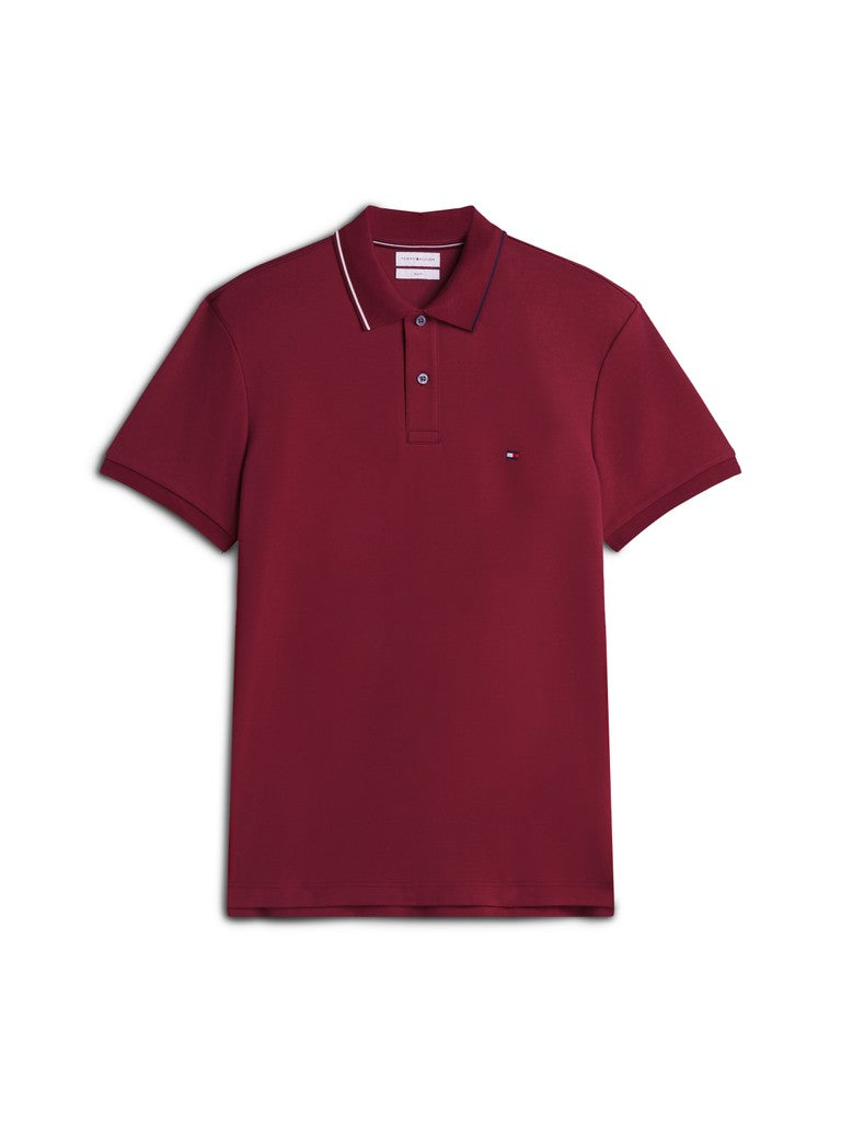 A short-sleeve polo shirt in deep burgundy, featuring a classic collar with thin white piping, a two-button placket, and a small embroidered Tommy Hilfiger flag logo on the left chest, displayed on a clean white background.