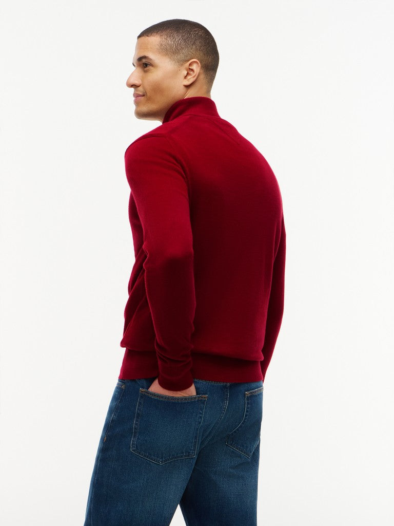 A man wearing a deep red mock neck knit sweater and blue jeans, shown from a side-back profile against a plain white studio background.