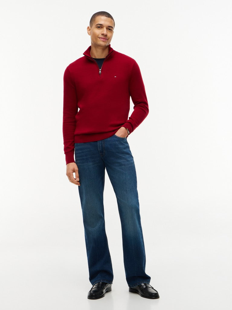 A man modeling a red quarter-zip knit sweater and blue jeans against a plain white studio background.