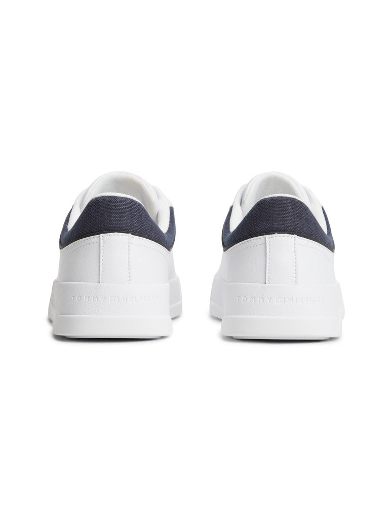A pair of white low-top sneakers shown from the back, featuring navy blue fabric heel tabs and white soles with 'Tommy Hilfiger' debossed on the back of the sole.