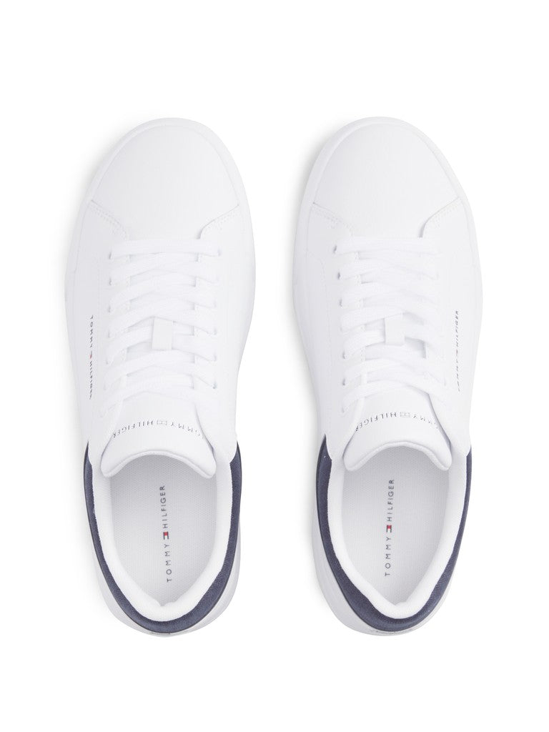 A pair of white low-top sneakers shown from a top-down view on a clean white background. The shoes feature white leather uppers with white laces, a navy blue heel tab, and the Tommy Hilfiger logo printed on the insole.