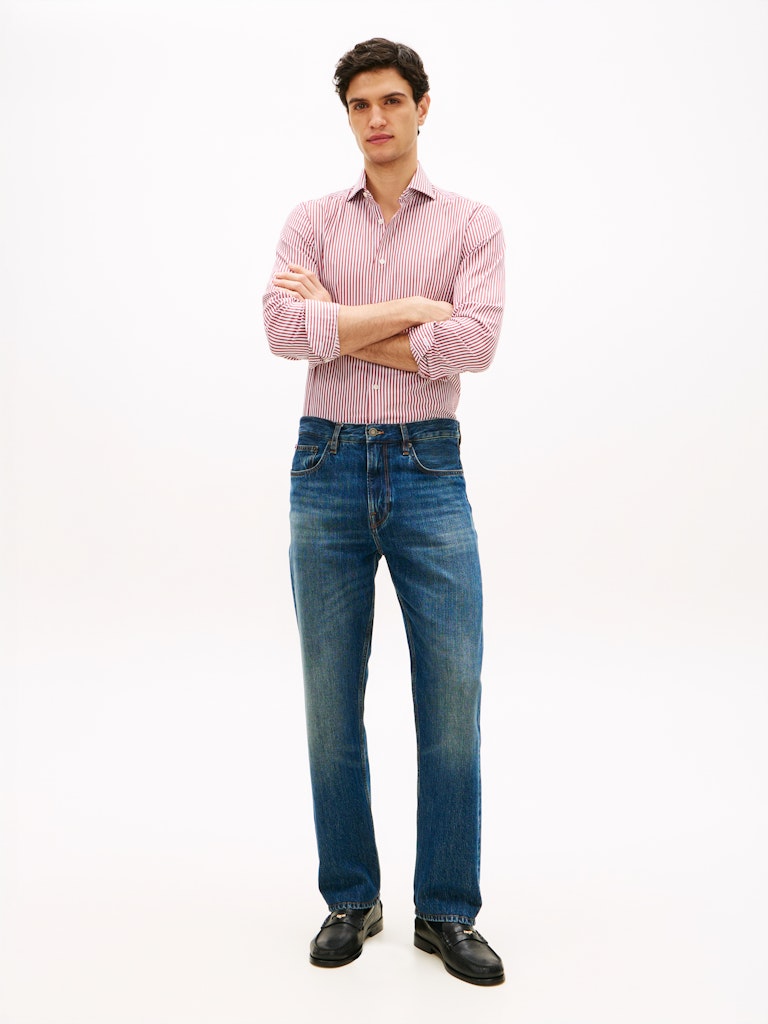 Man wearing a pink shirt and blue jeans standing against a white background