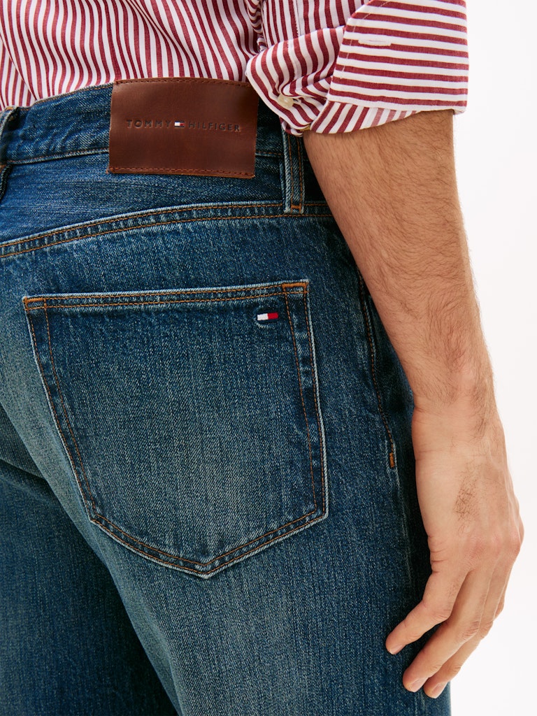 Close-up of blue jeans with a Tommy Hilfiger brand logo, worn by a man.