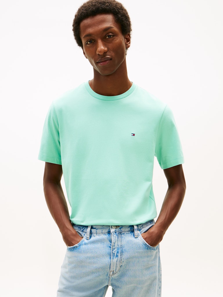 Man wearing a light green t-shirt with small Tommy Hilfiger logo and light blue jeans on a white background