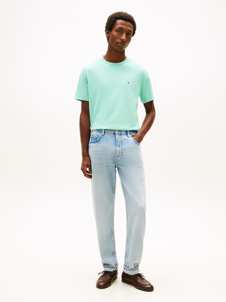 Man wearing a light green t-shirt and light blue jeans on a white background
