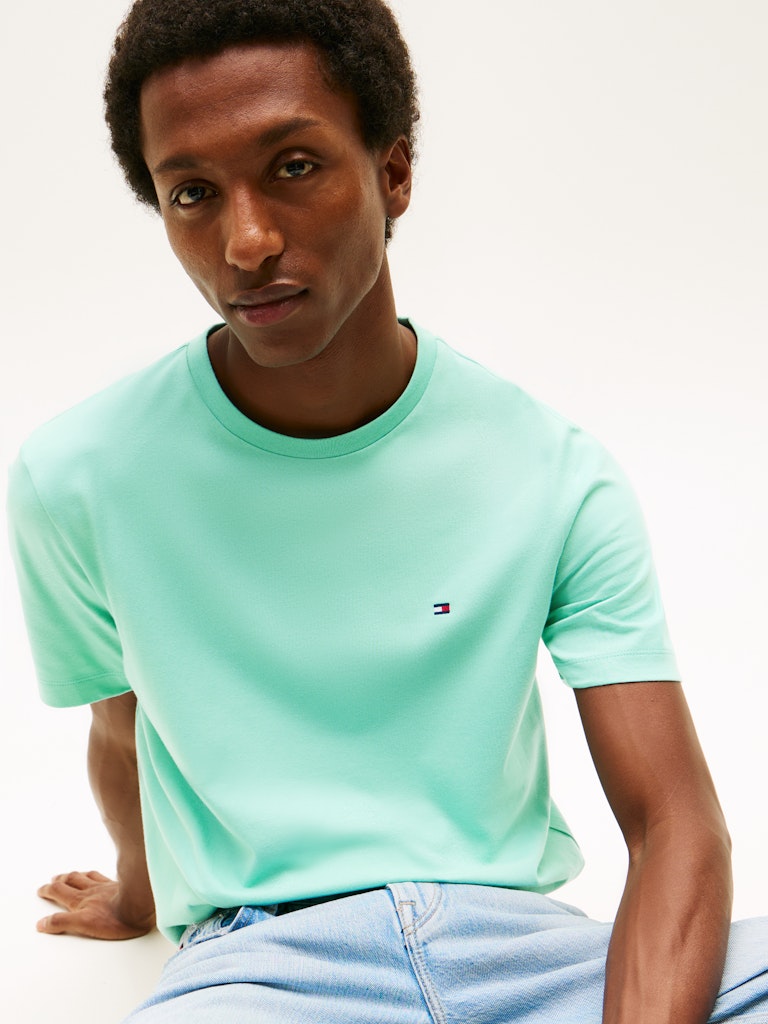 Man wearing a light blue t-shirt with a small logo, sitting against a white background