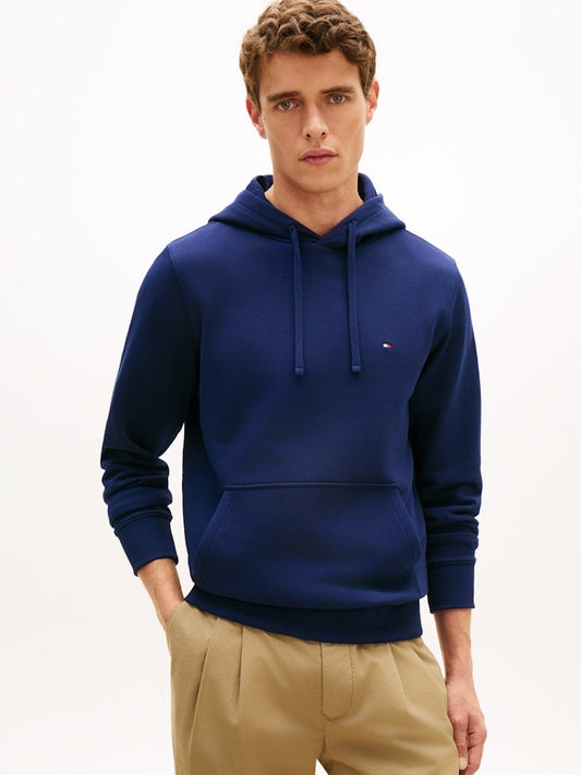 Man wearing a blue hoodie with a Tommy Hilfiger brand logo on a white background