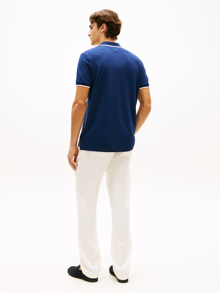 Man wearing a blue polo shirt and white pants on a white background