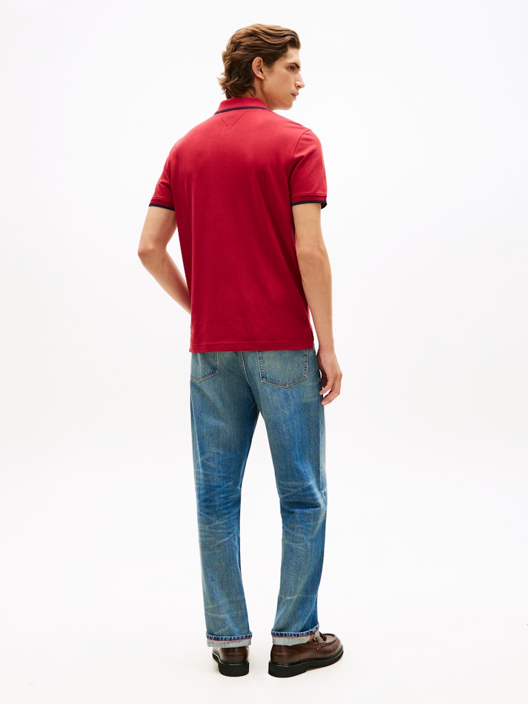 Man wearing a red polo shirt and blue jeans on a white background
